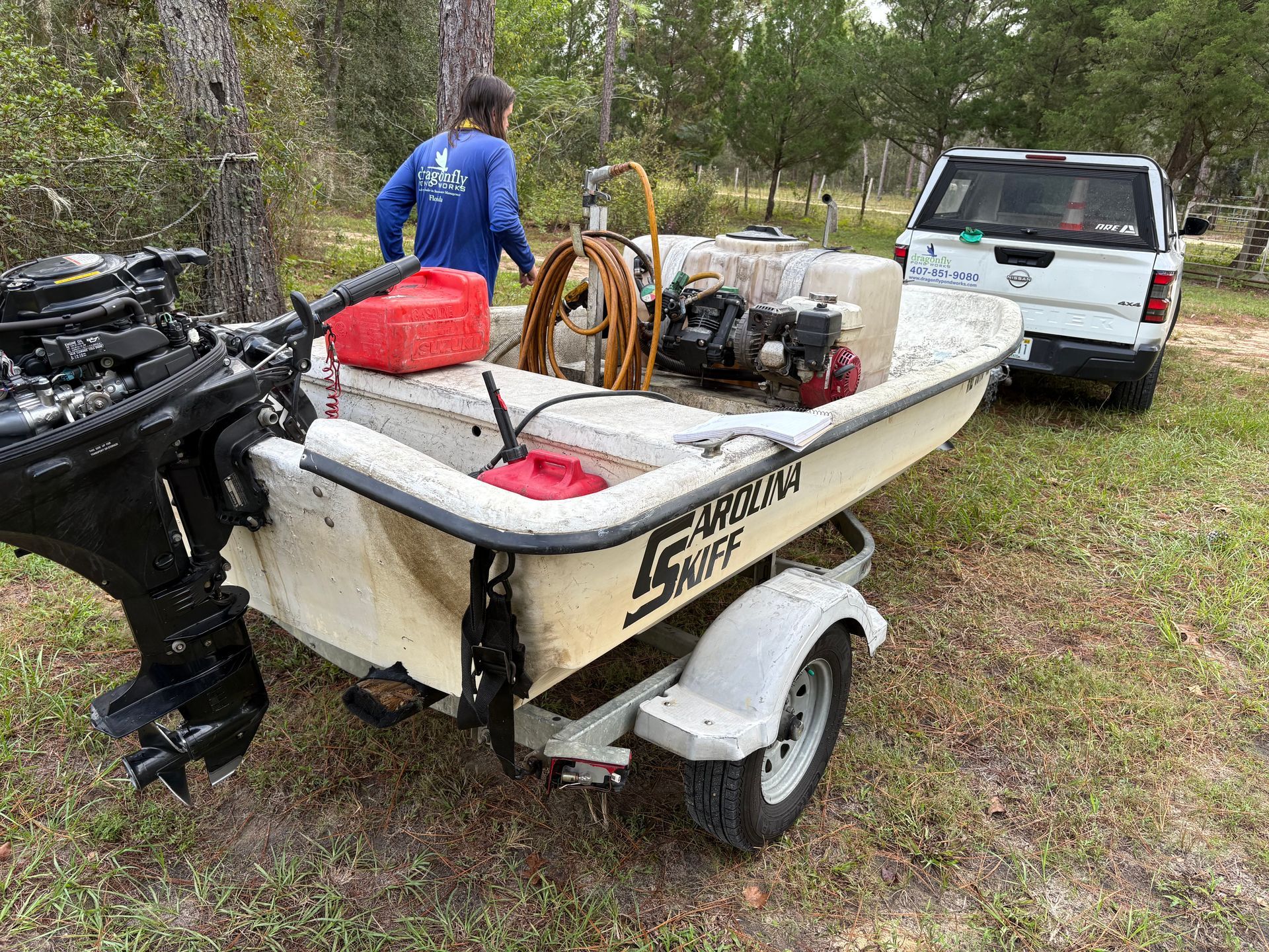 Boat on trailer with person, fuel cans, and equipment near a white truck.