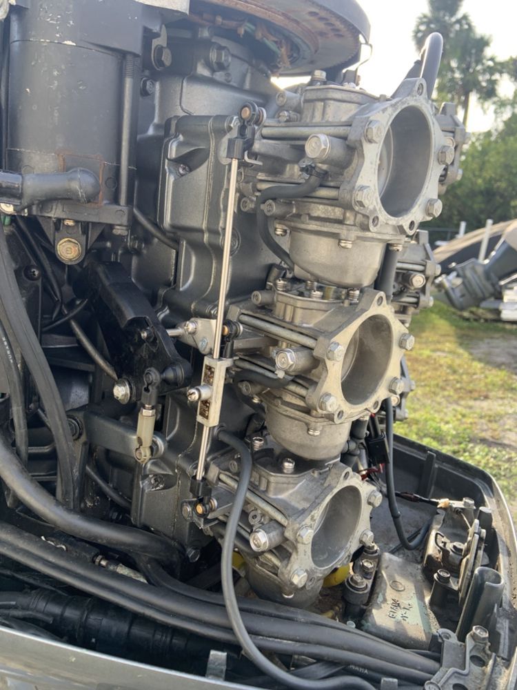 Close-up of a three-cylinder outboard motor with carburetors, hoses, and mechanical components.