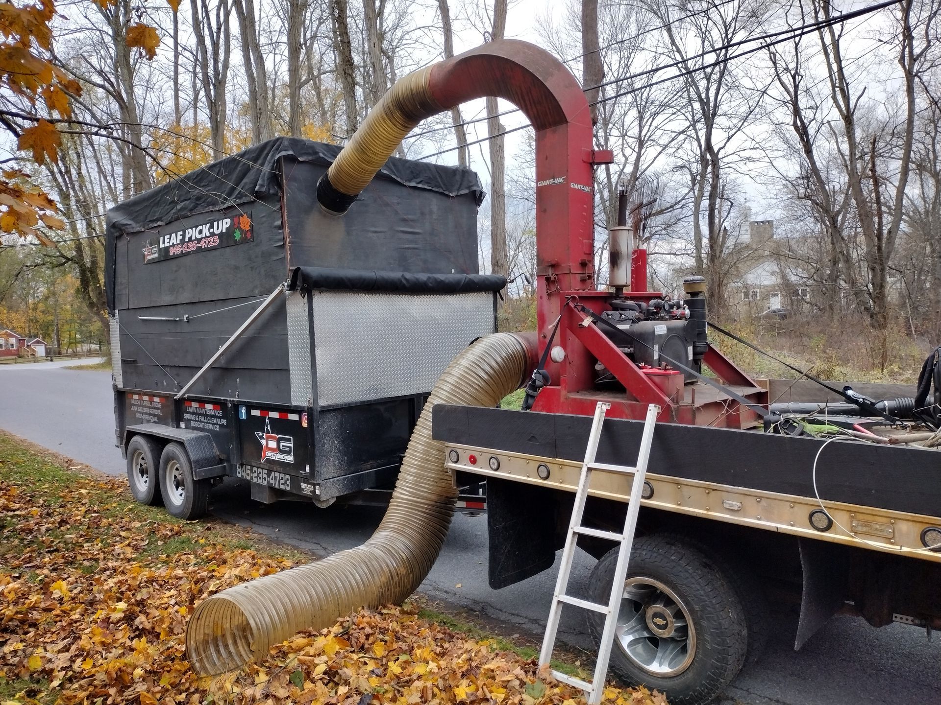 Leaf vacuum machine with trailer on a road collecting fallen leaves. Leaf vacuum machine with trailer on a road collecting fallen leaves.