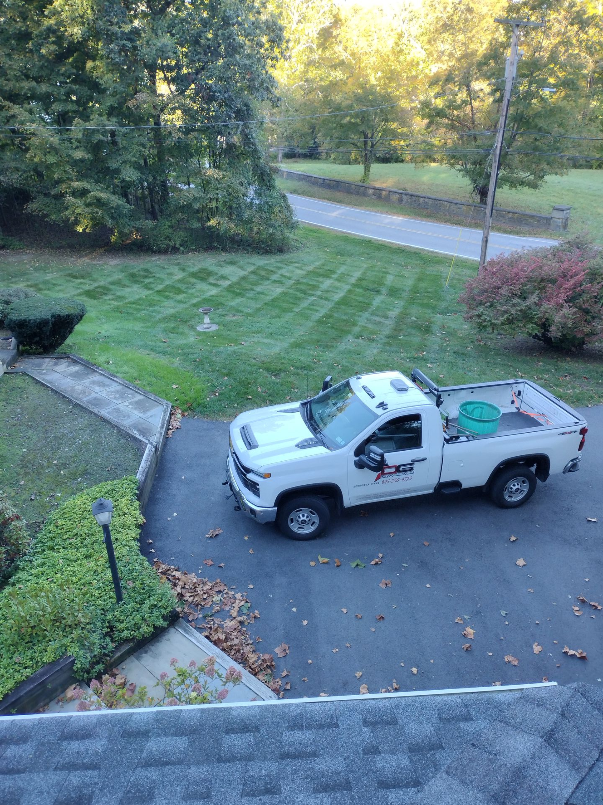 White truck parked on a driveway, next to a manicured lawn. Trees and a road are visible in the background.