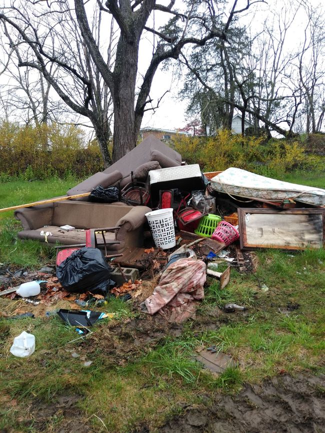 Pile of trash including furniture and bags on a muddy grassy area.