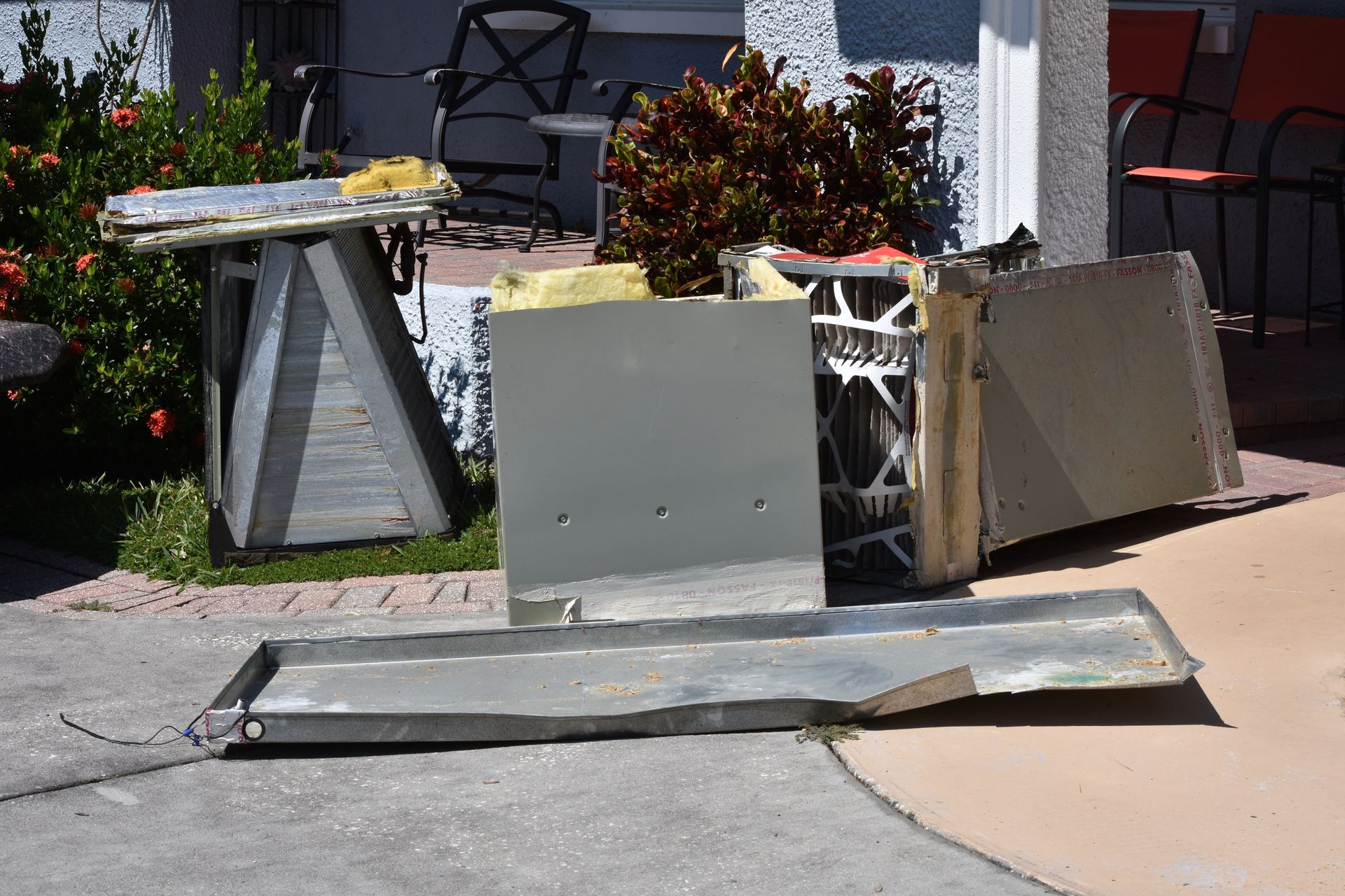 Deconstructed air conditioner parts laid out on pavement outside a house.