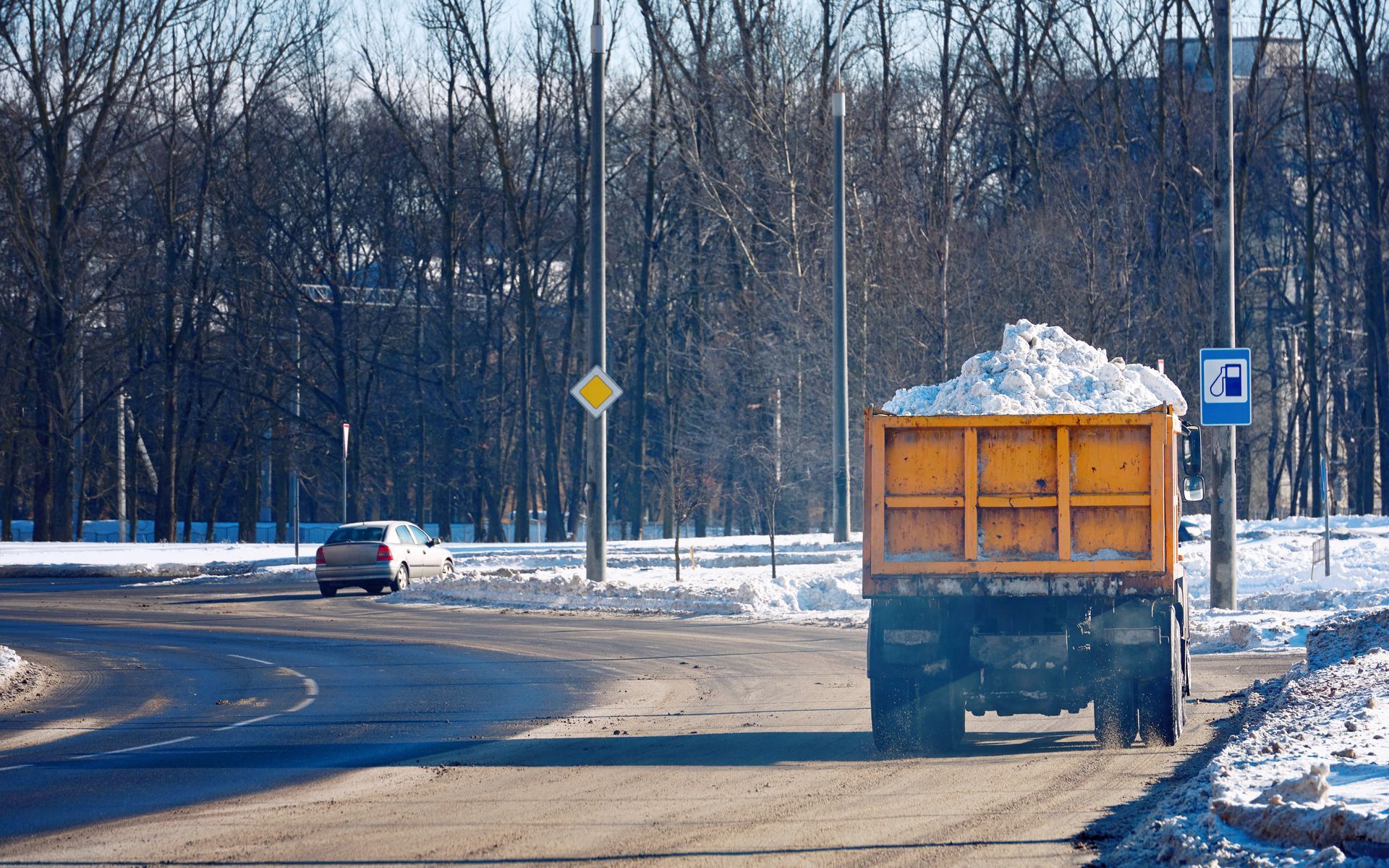 Snow-covered dump truck on a road, trees in background, small car in distance. Snow-covered dump truck on a road, trees in background, small car in distance.