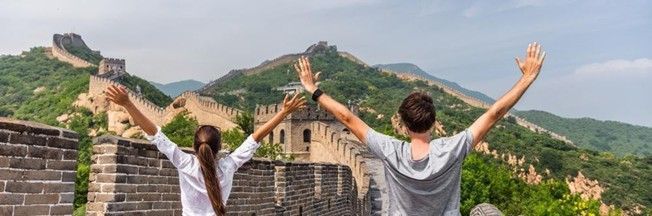 A man and a woman are standing on the great wall of china with their arms outstretched.