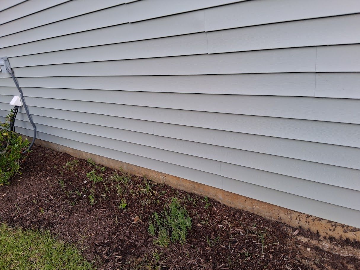 A man is cleaning a brick house with a pressure washer.