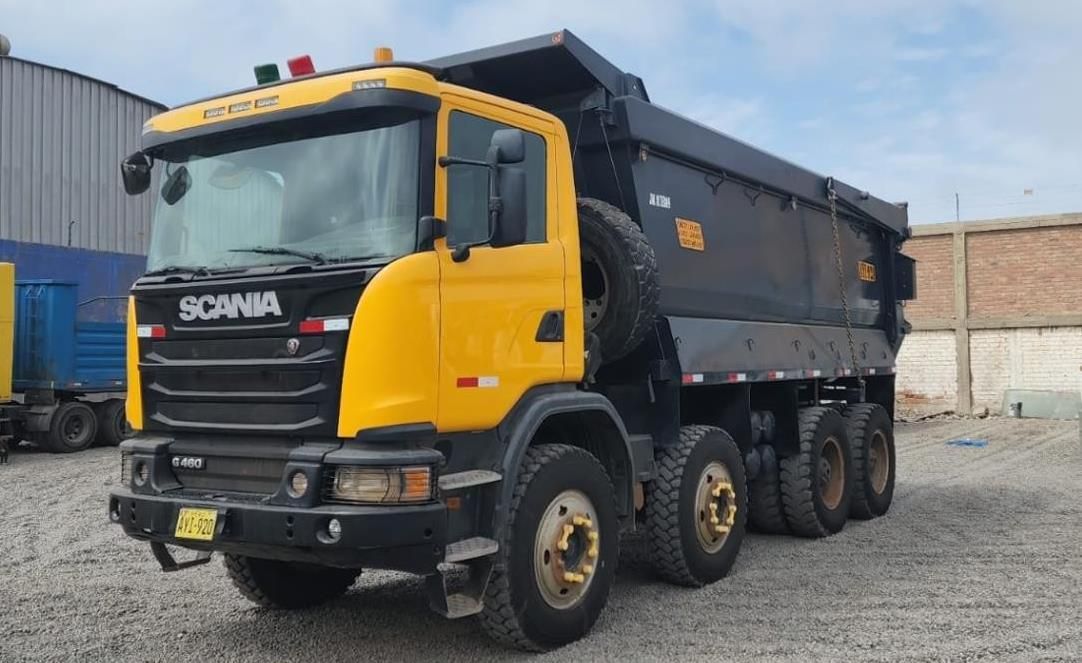Camión volquete Scania amarillo estacionado sobre grava en un patio industrial.