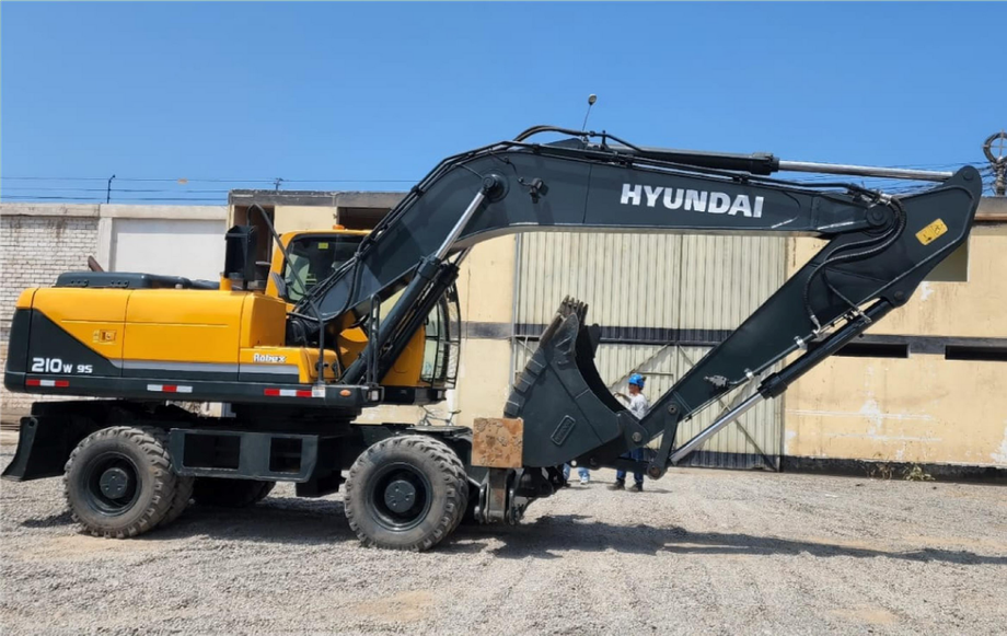Excavadora Hyundai amarilla y negra estacionada sobre grava junto a un almacén bajo un cielo azul.