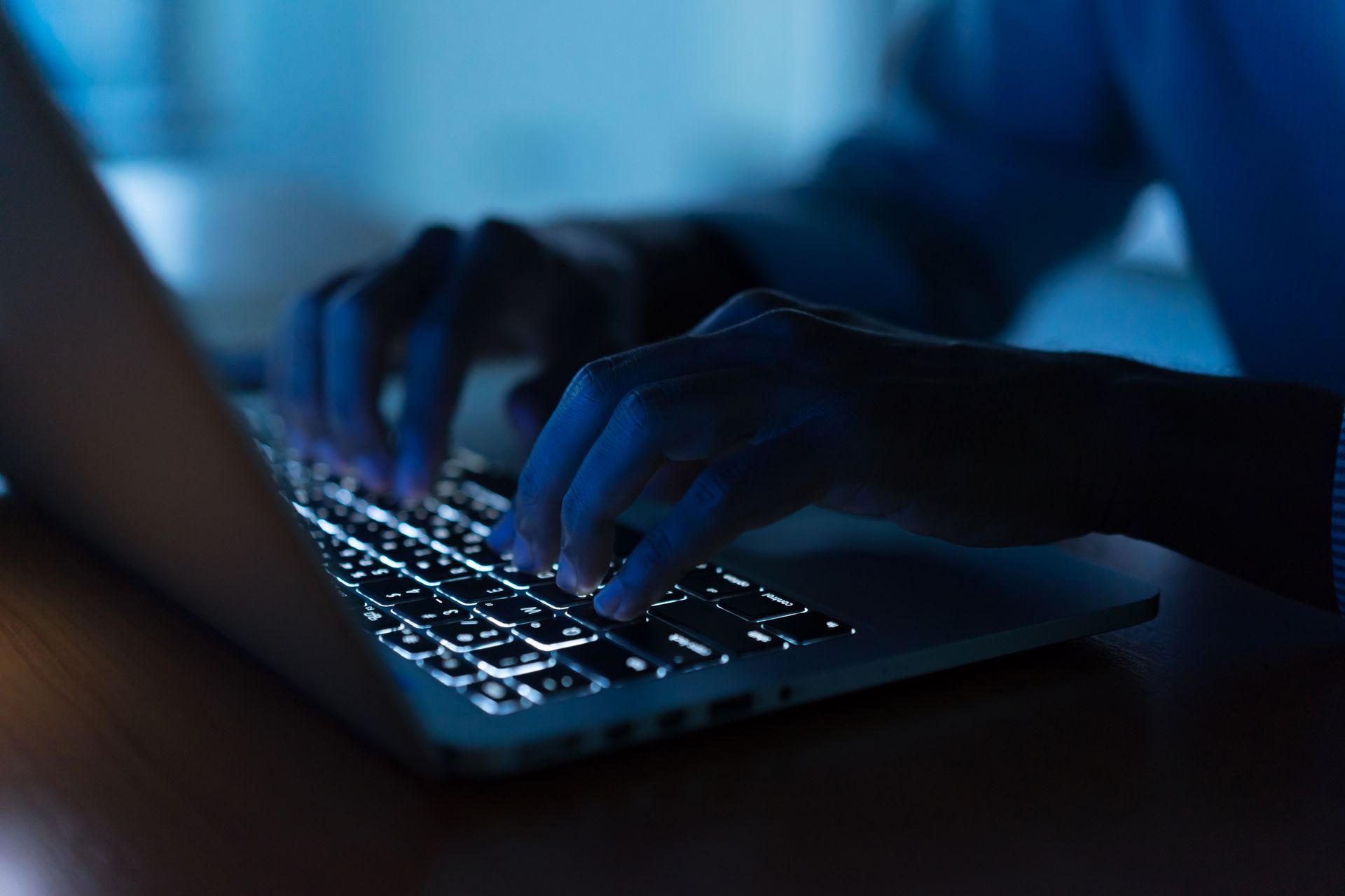A person typing on a laptop. Dark lighting.