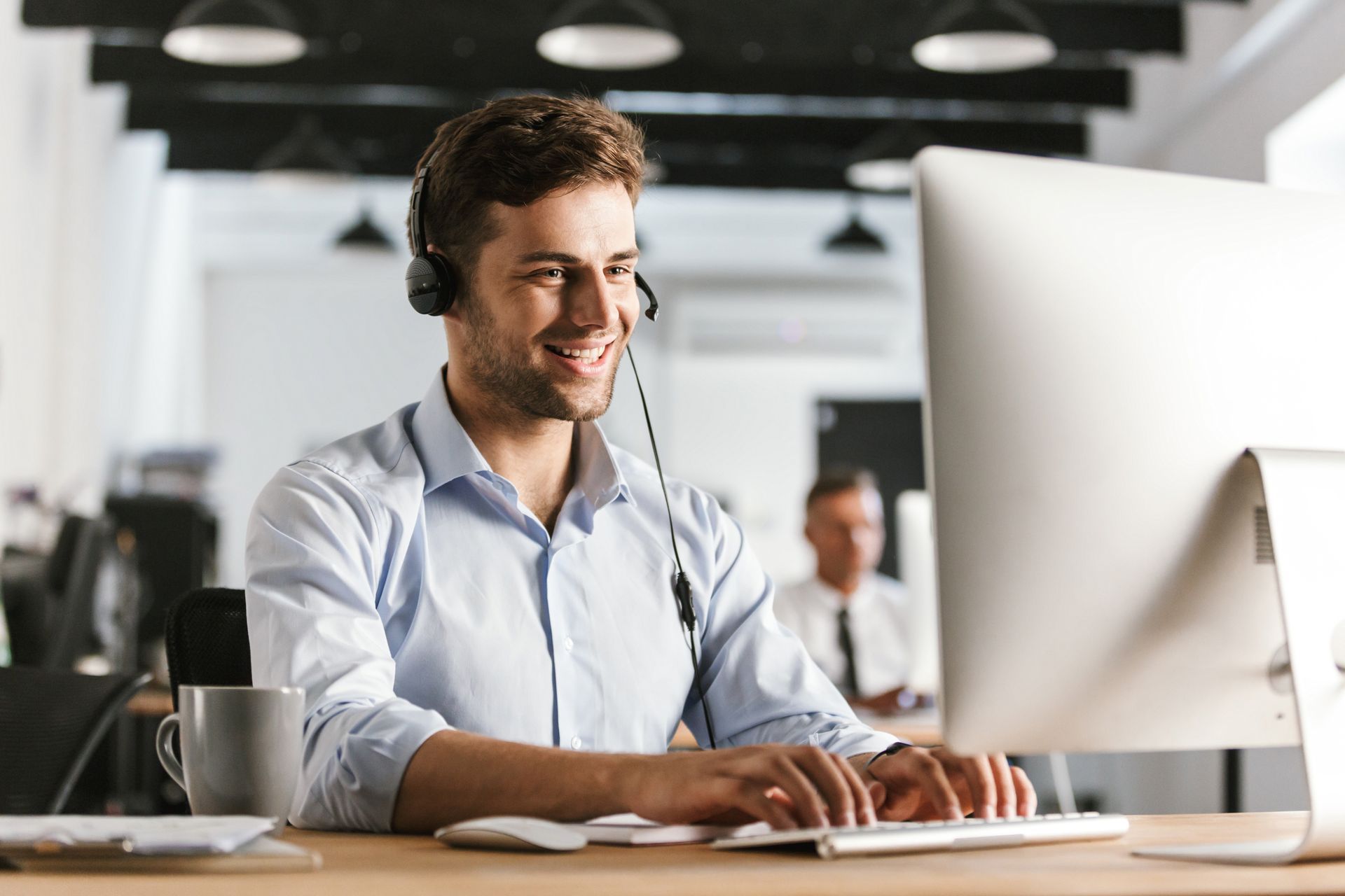 Man working at a computer with headset plugged in, he is typing.