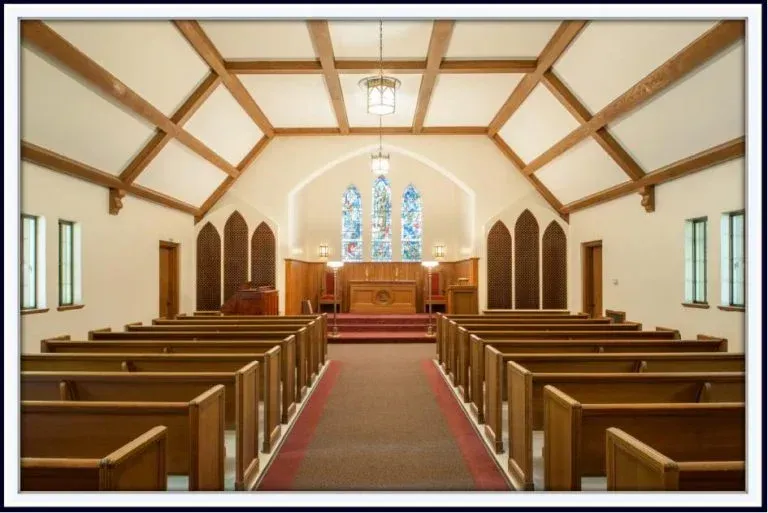A church with rows of wooden benches and a stained glass window