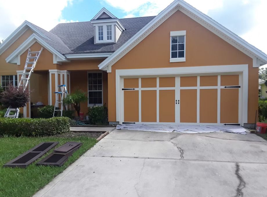 House exterior being painted orange with white trim, garage door, and a ladder.