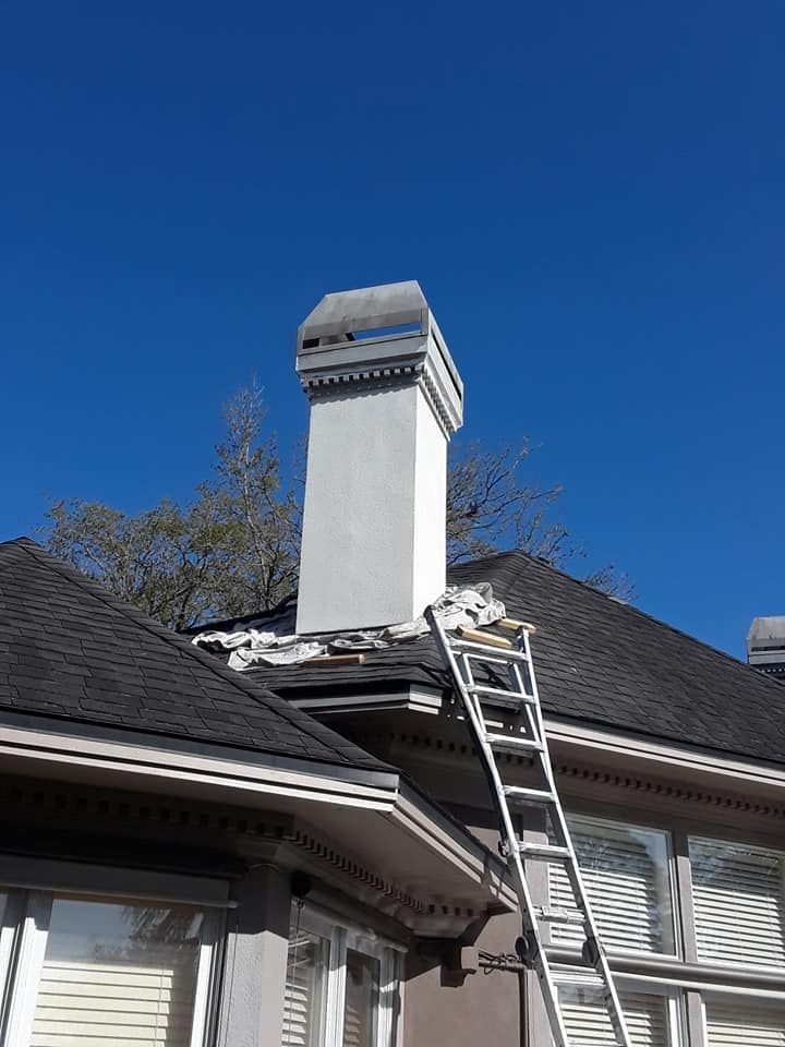 Ladder leaning against roof near a white chimney with a cap; bright blue sky.