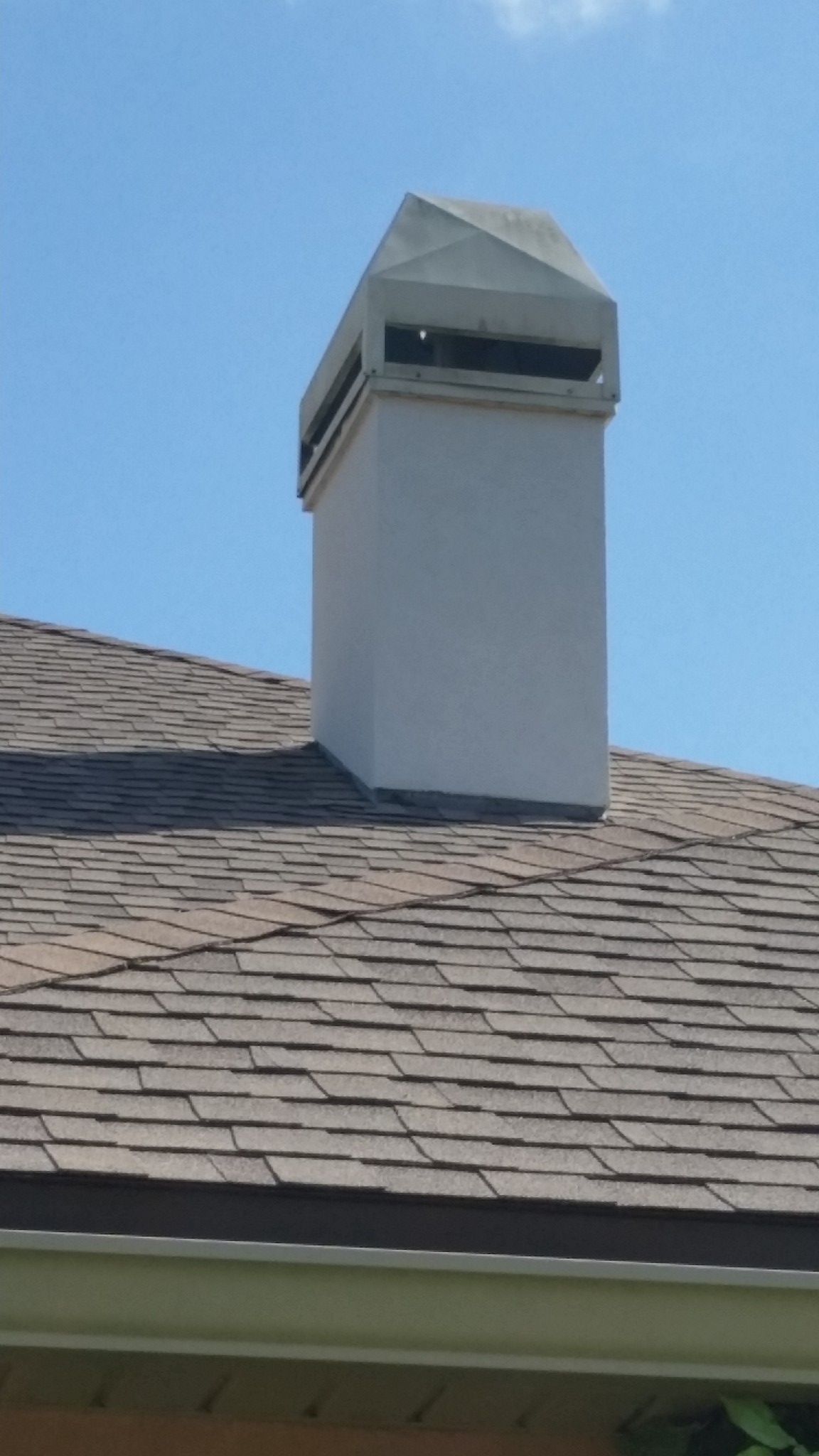 White chimney with a capped top on a brown shingled roof, against a blue sky.