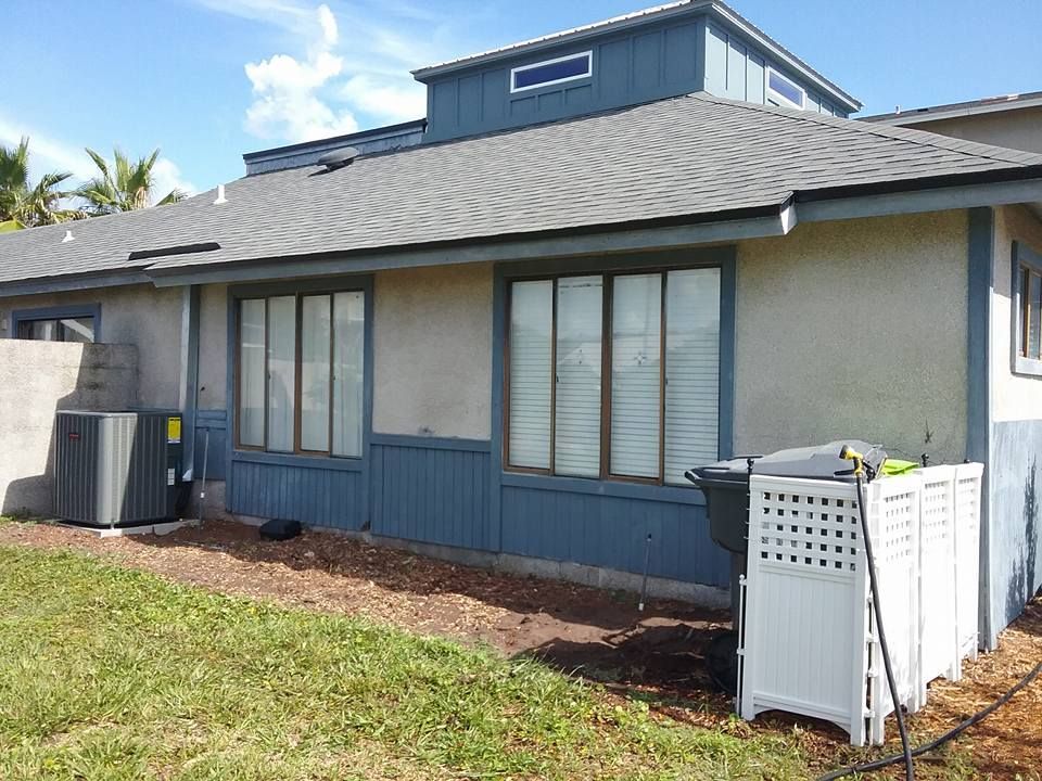 Exterior view of a house with blue trim, windows, and an air conditioning unit.