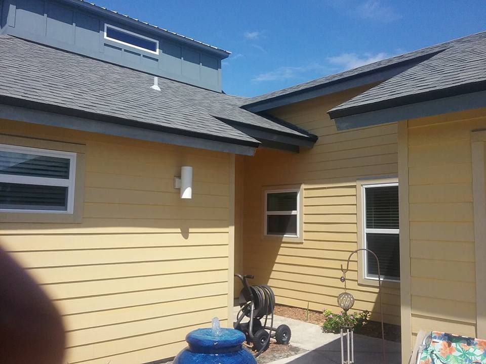 Yellow house with blue roof and white windows under a blue sky.