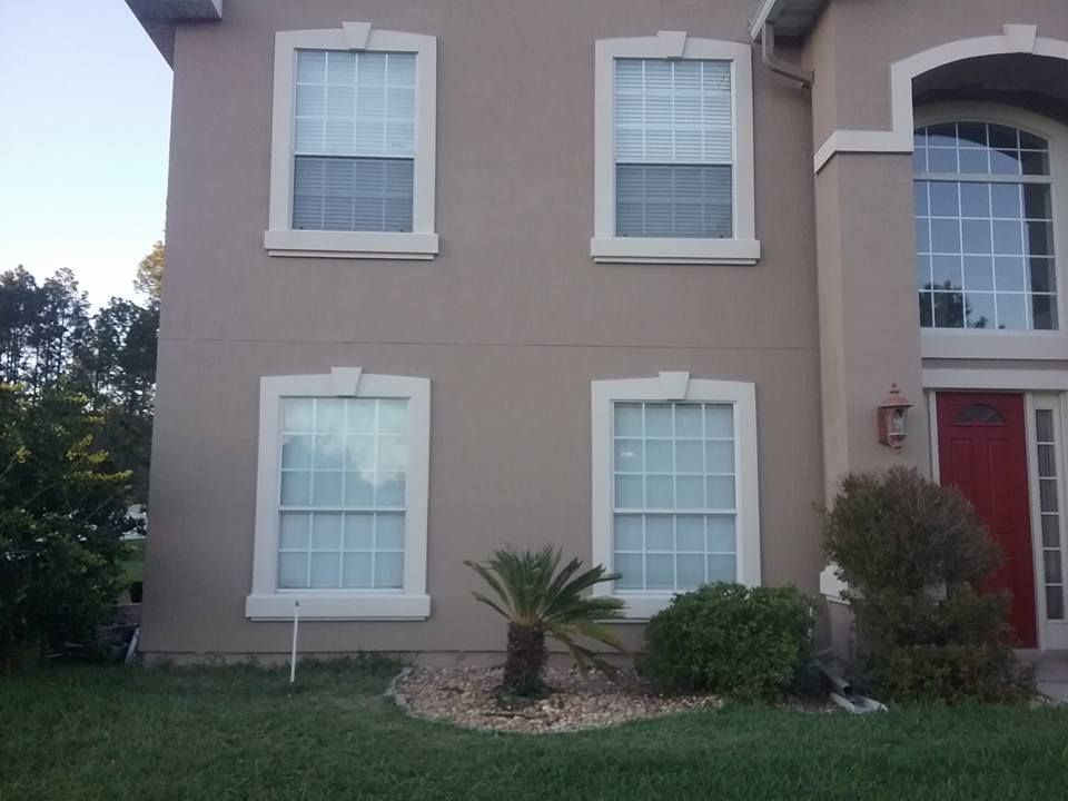 Tan house with white-trimmed windows and a red door, a small palm tree in front.