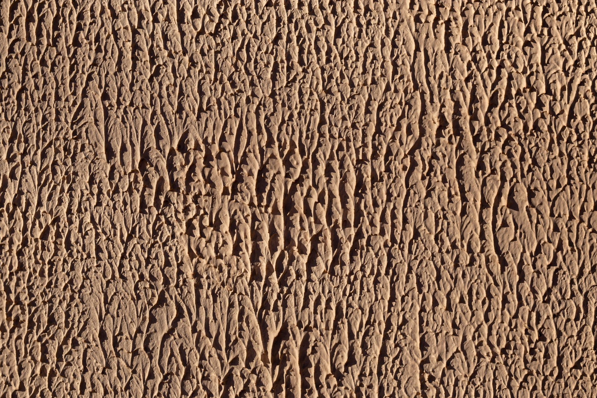 Textured tan stucco wall with vertical, rough pattern.