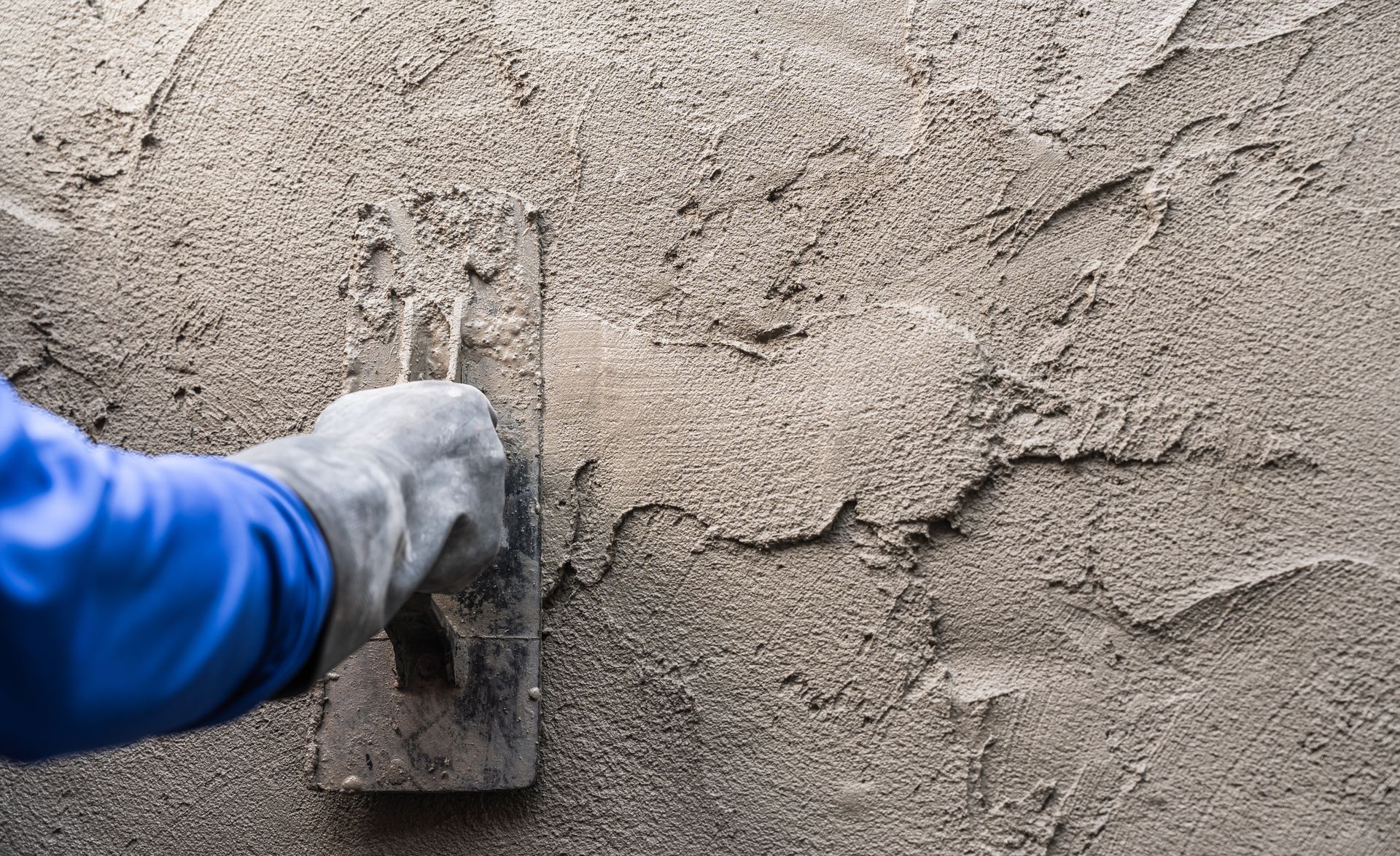 Gloved hand using a trowel to apply wet cement to a wall.