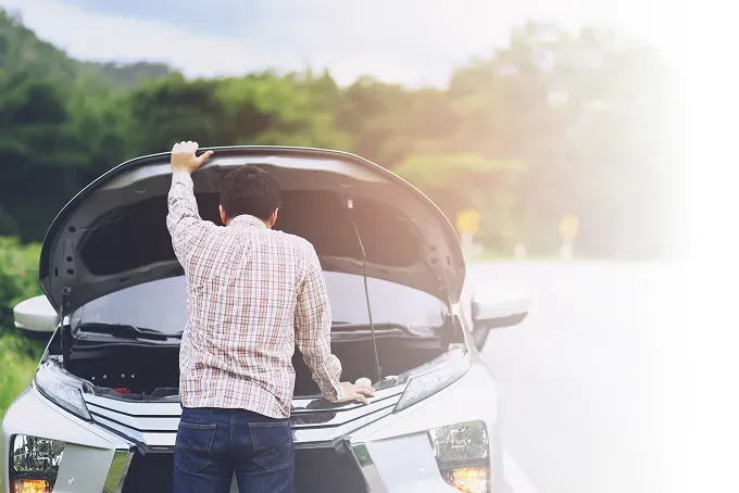 Man looking at engine inside hood of car pulled over on the side of the road | Four Seasons Tire & Auto Service