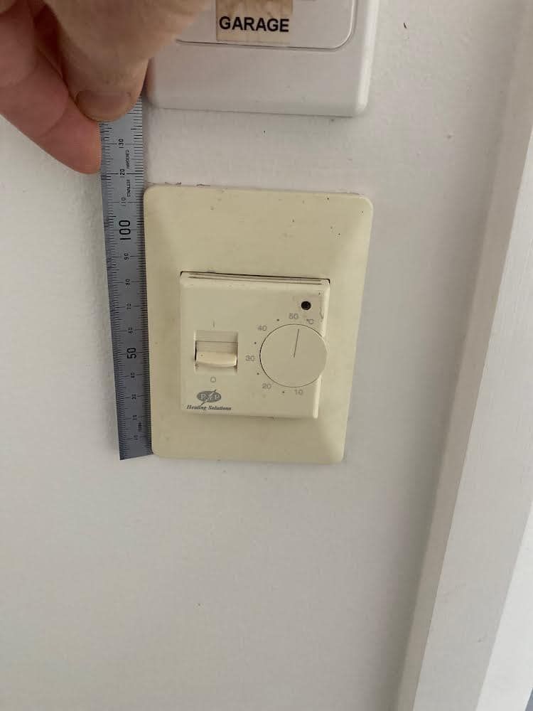 A person is measuring a thermostat with a ruler.