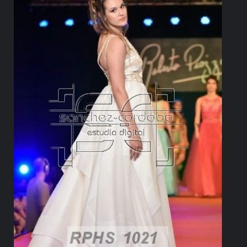 Una mujer con un vestido blanco camina por la pasarela durante un desfile de moda.