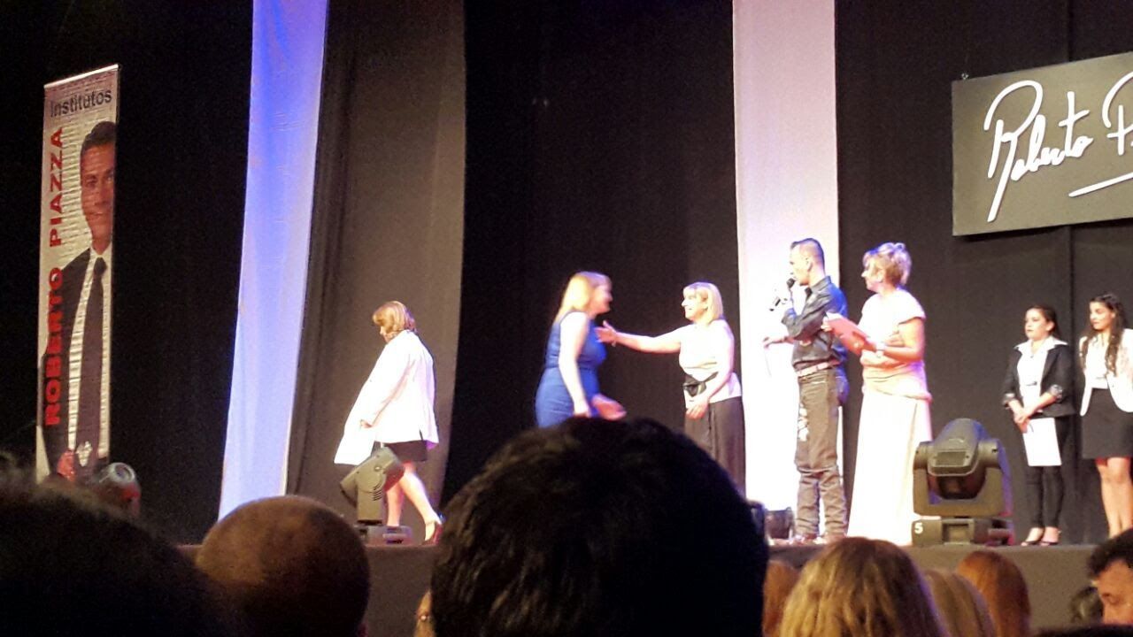 Personas en un escenario, algunas recibiendo ayuda o abrazos. A la izquierda, una pancarta con el rostro de un hombre.