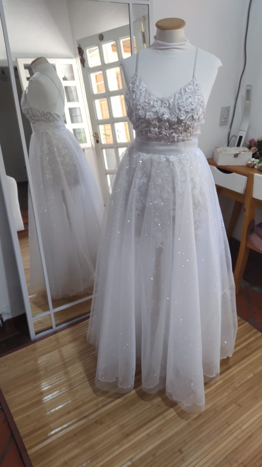 Un vestido de novia blanco está sobre un maniquí frente a un espejo.