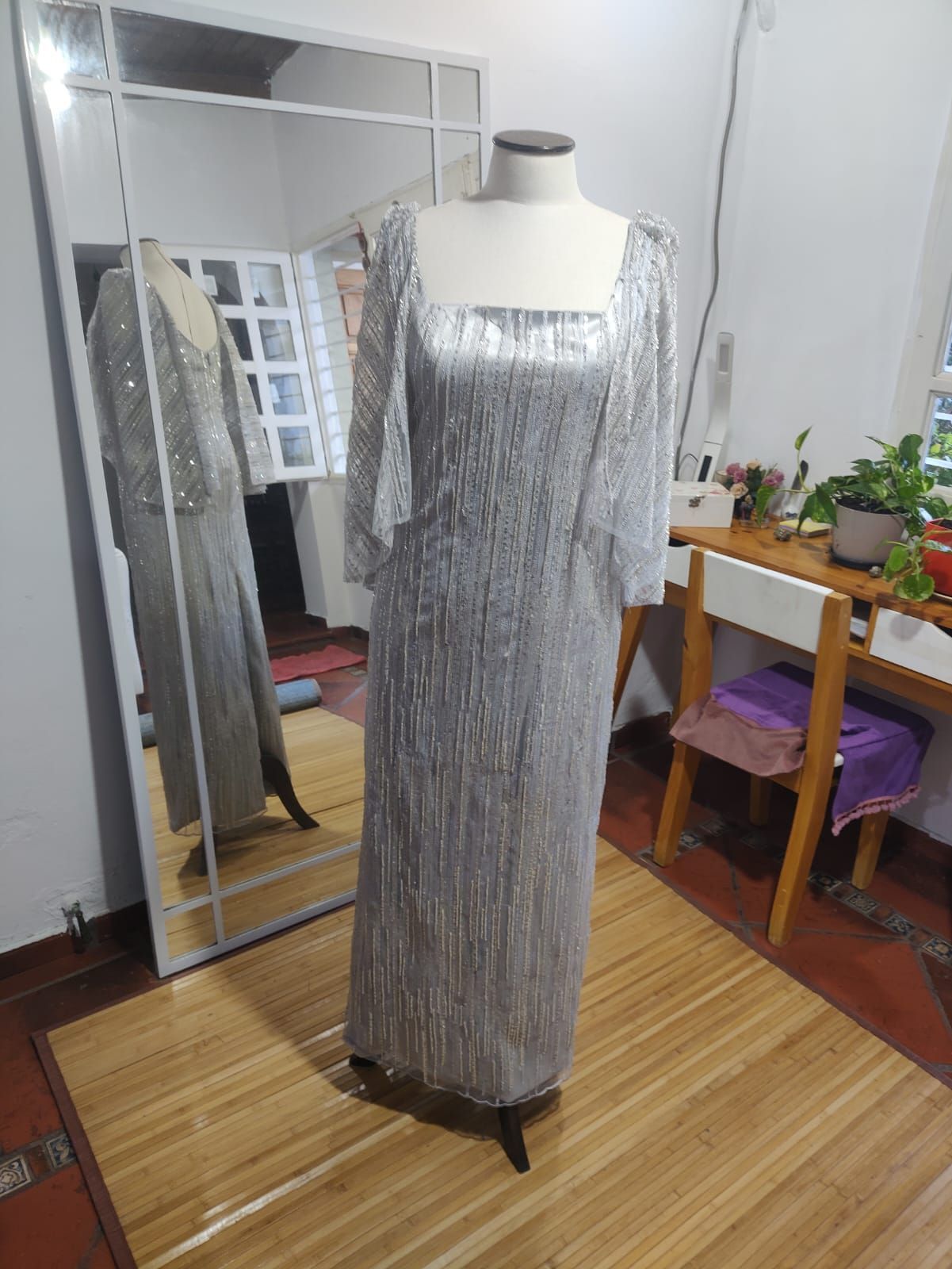 Un maniquí lleva un vestido largo plateado frente a un espejo.