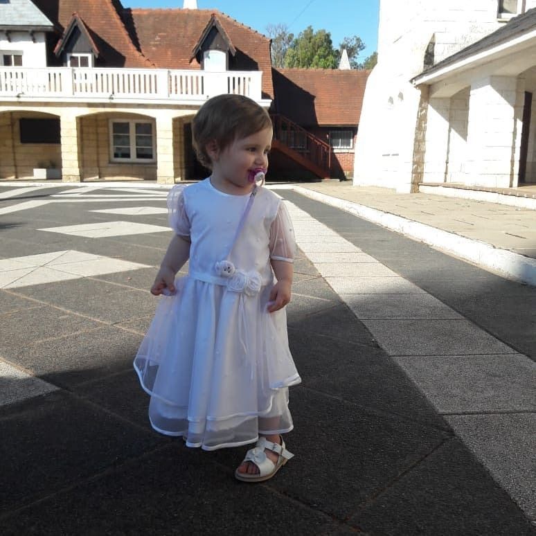 Una niña con un vestido blanco y un chupete en la boca.