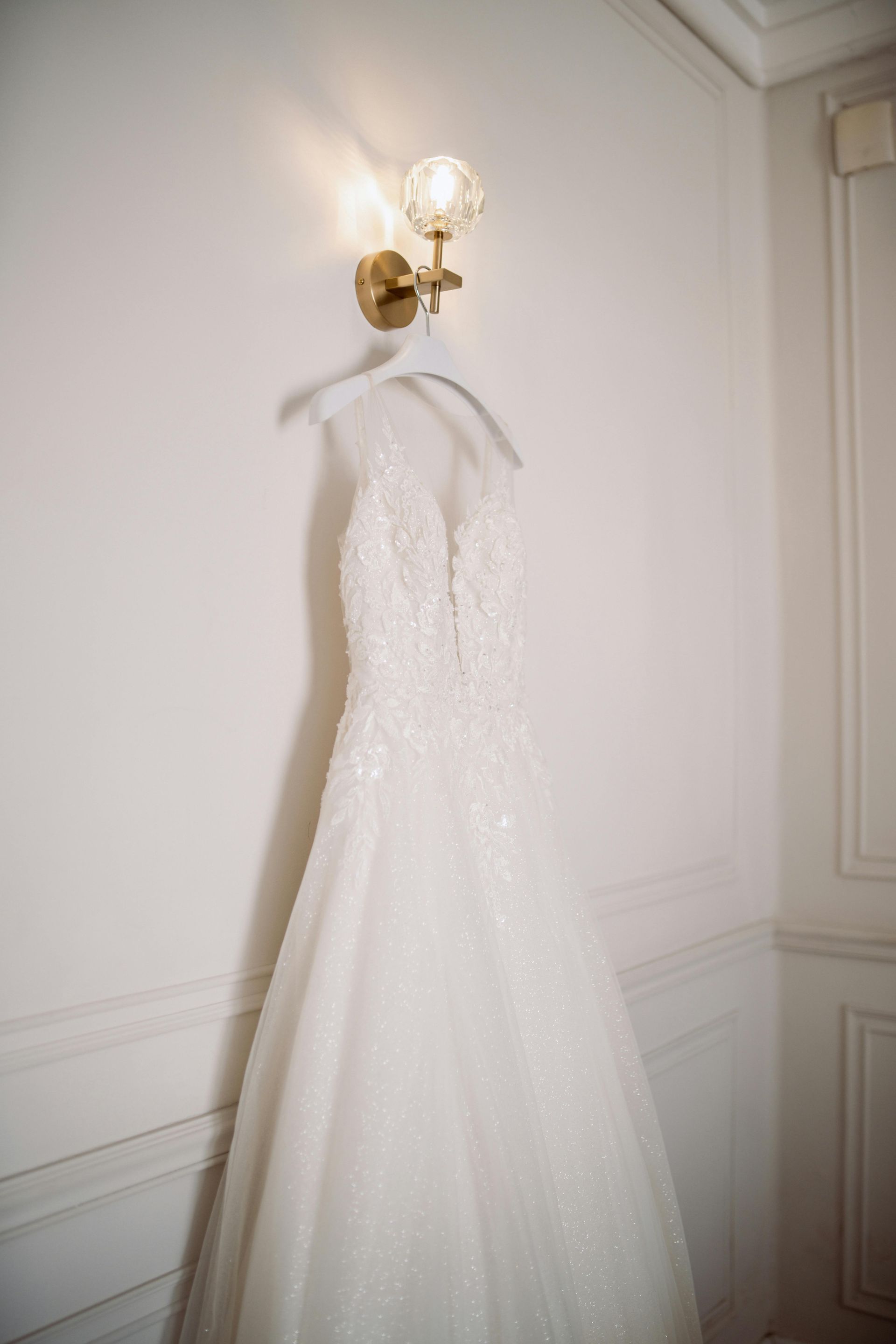 Vestido de novia blanco colgado en una pared bajo un aplique dorado.