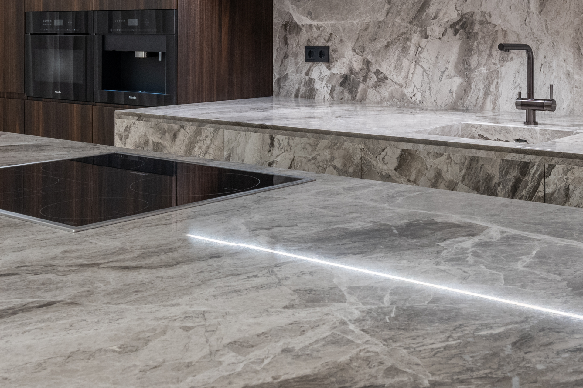 A kitchen with a sink , stove top oven , and marble counter tops.