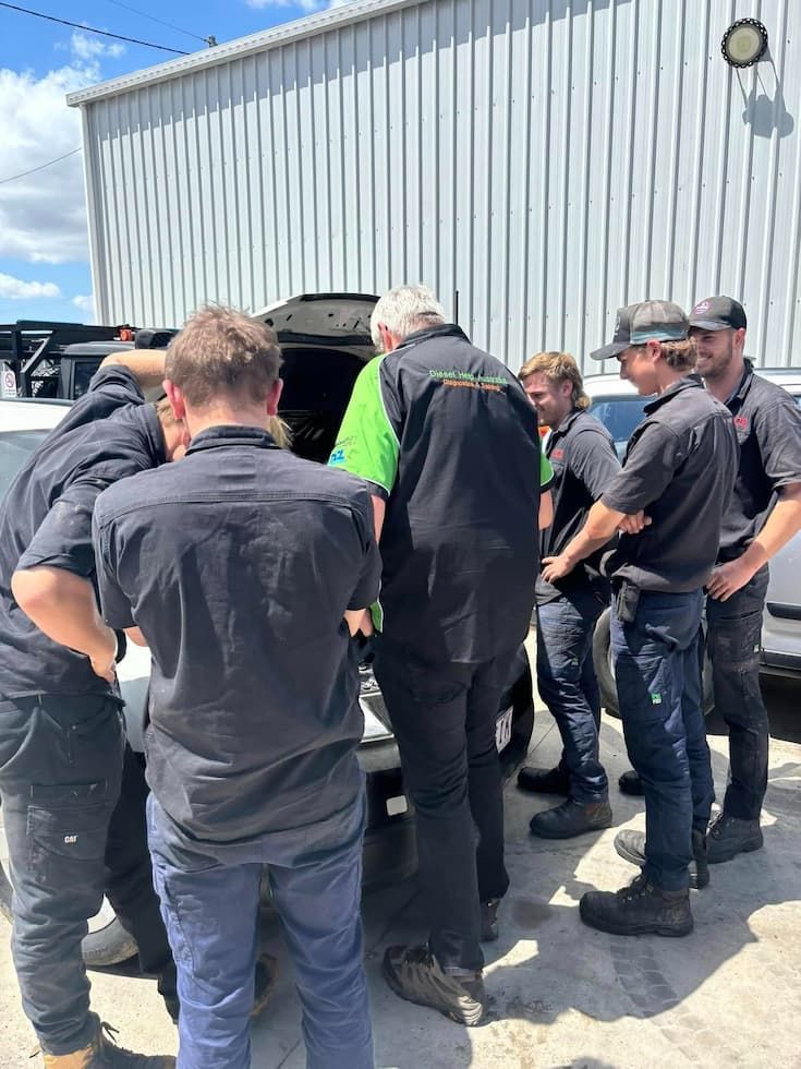 A Group of Mechanics Gather Around an Open Car Hood, Focusing Intently on the Engine