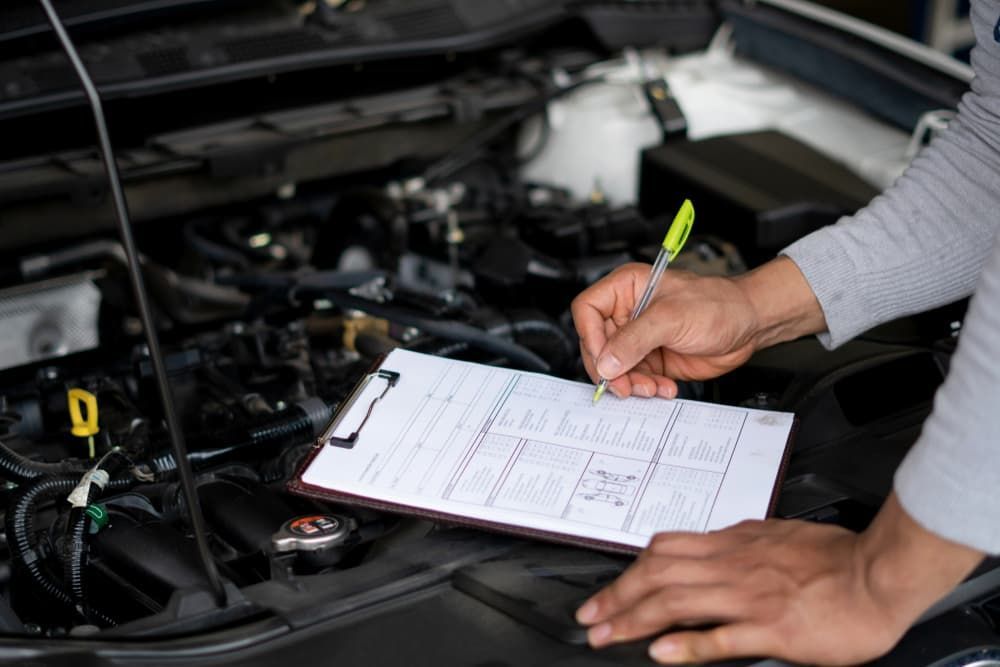 Mechanic in Gray Sleeve Makes Notes on a Clipboard While Inspecting a Car Engine
