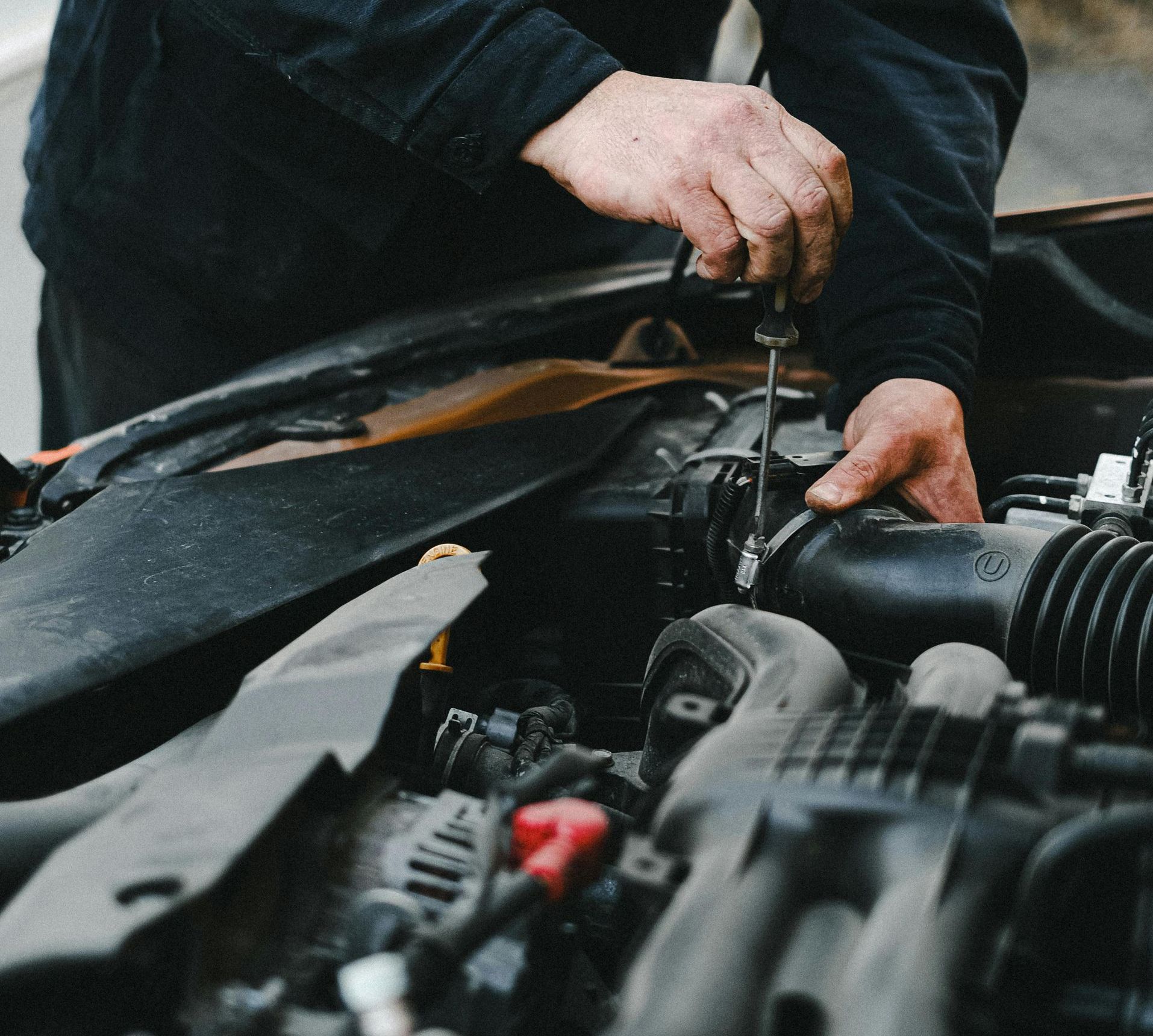 mechanic performing routine car servicing under the bonnet at an automotive workshop