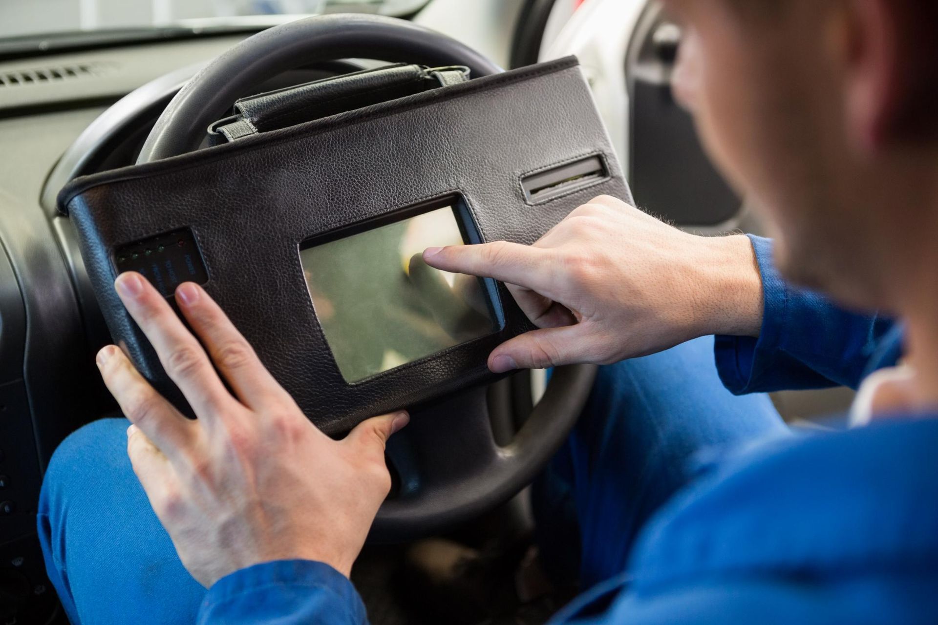 Person using a touchscreen device mounted on a car steering wheel inside a vehicle.