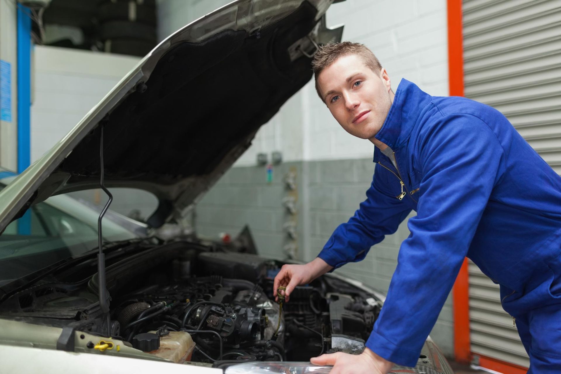 Mechanic in blue coveralls inspecting a car engine with the hood open in a garage