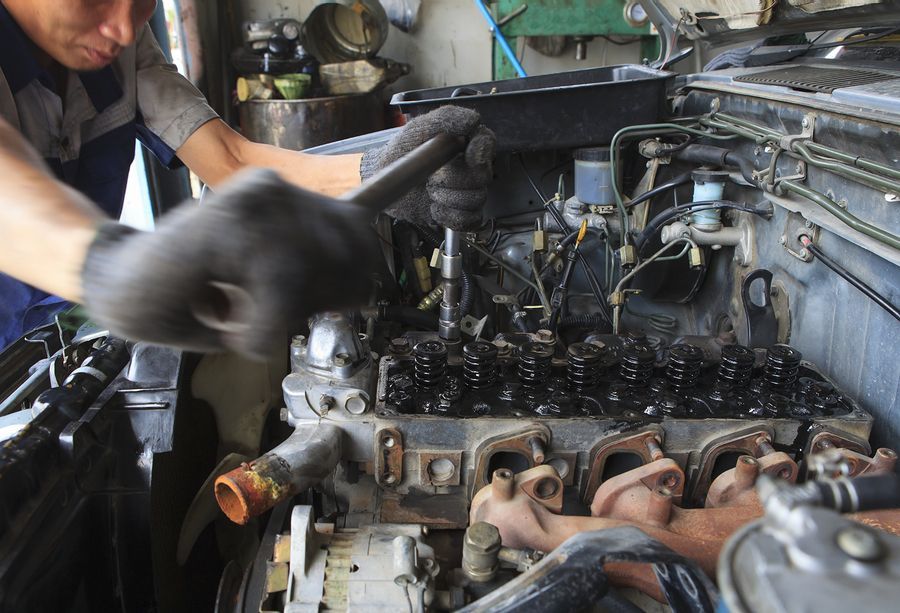 Mechanic working on a car engine bay with black-gloved hands and tools