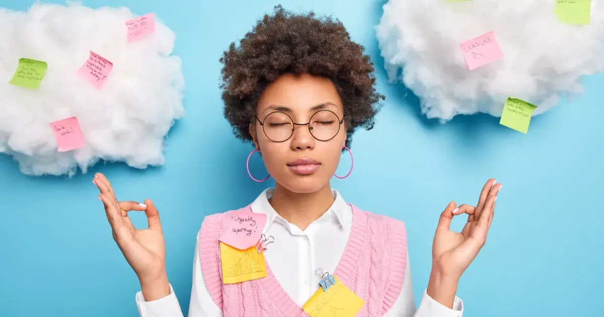 A woman is meditating with her eyes closed in front of clouds and sticky notes.