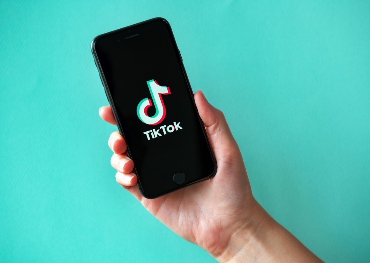 Hand holding a smartphone with the TikTok logo on a teal background
