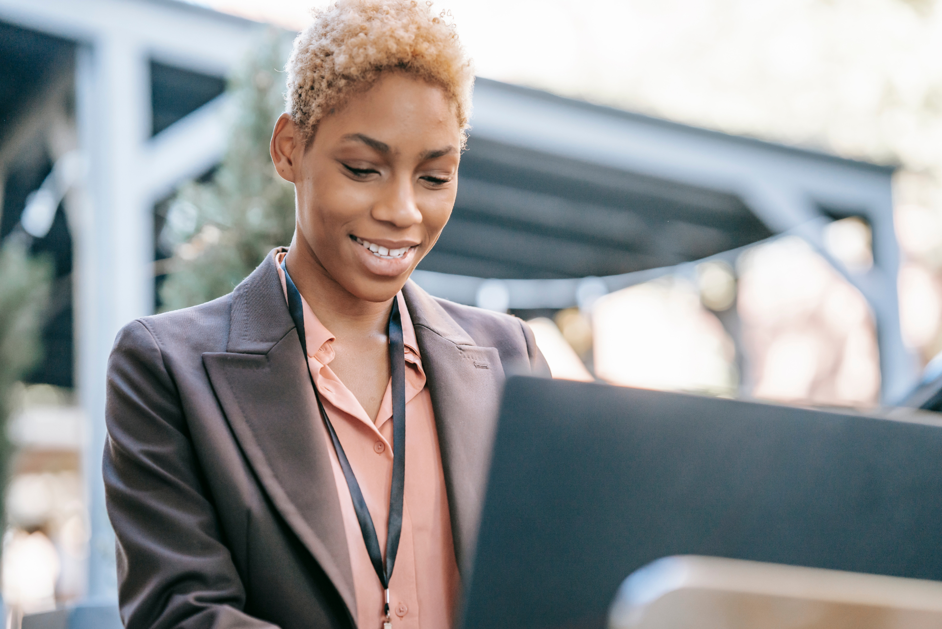 Woman with blonde hair smiles while working on a laptop outdoors.