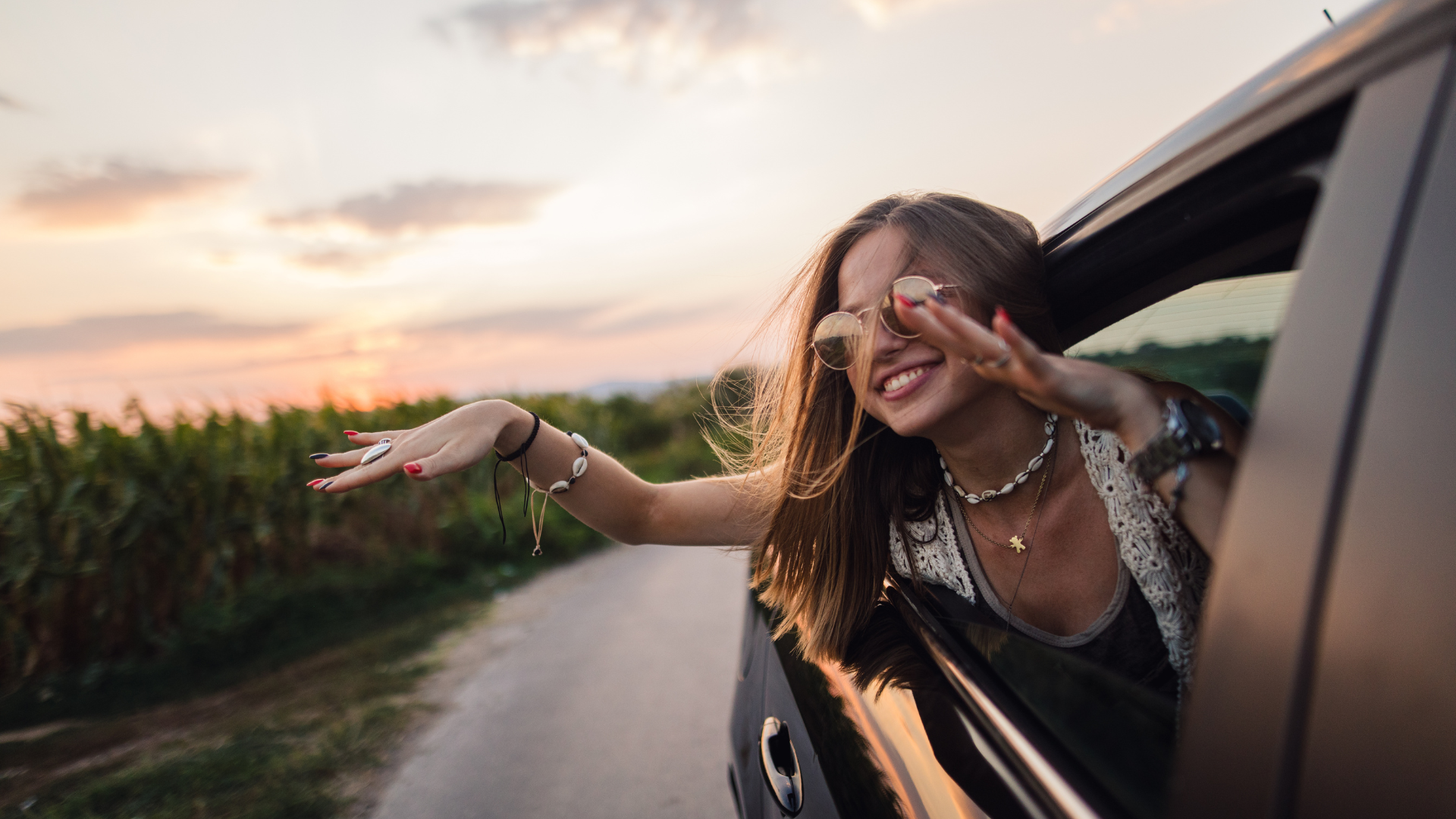 A woman is sticking her head out of a car window and smiling.
