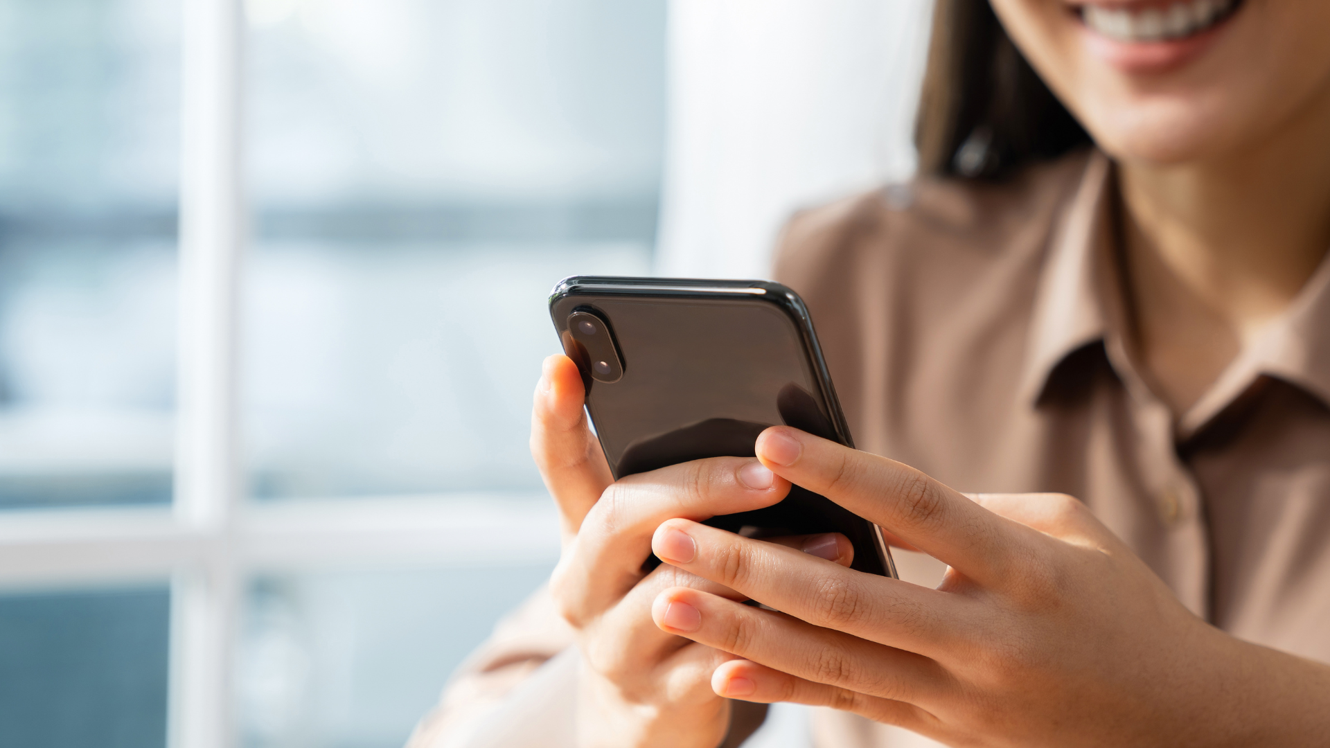 A woman is holding a cell phone in her hands and smiling.