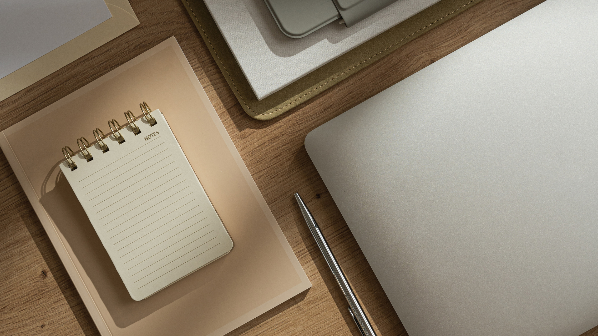 Notebook, laptop, and pen on a wooden desk; a workspace.