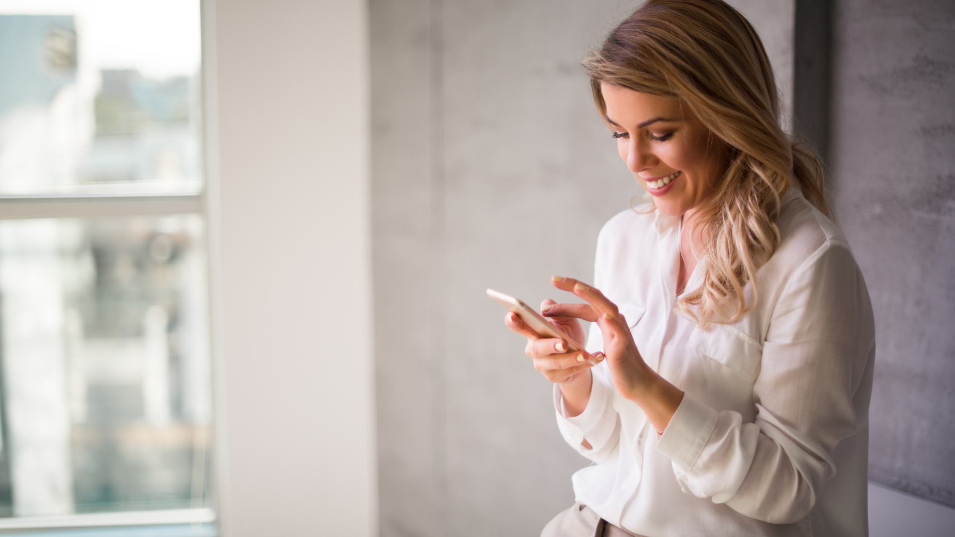 Woman smiling while using a smartphone in an office setting.