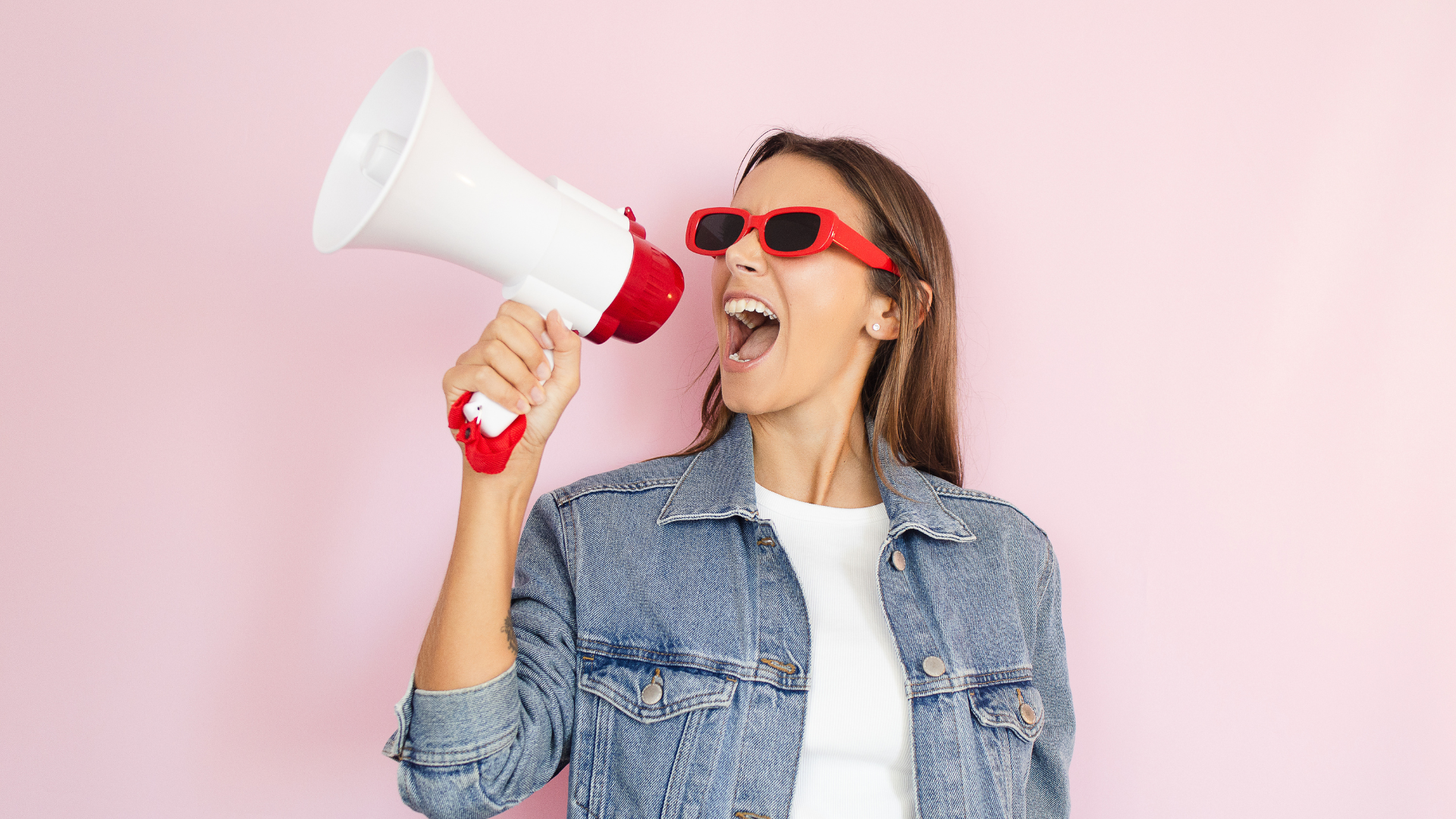 Woman in sunglasses yelling into a megaphone against a pink background.