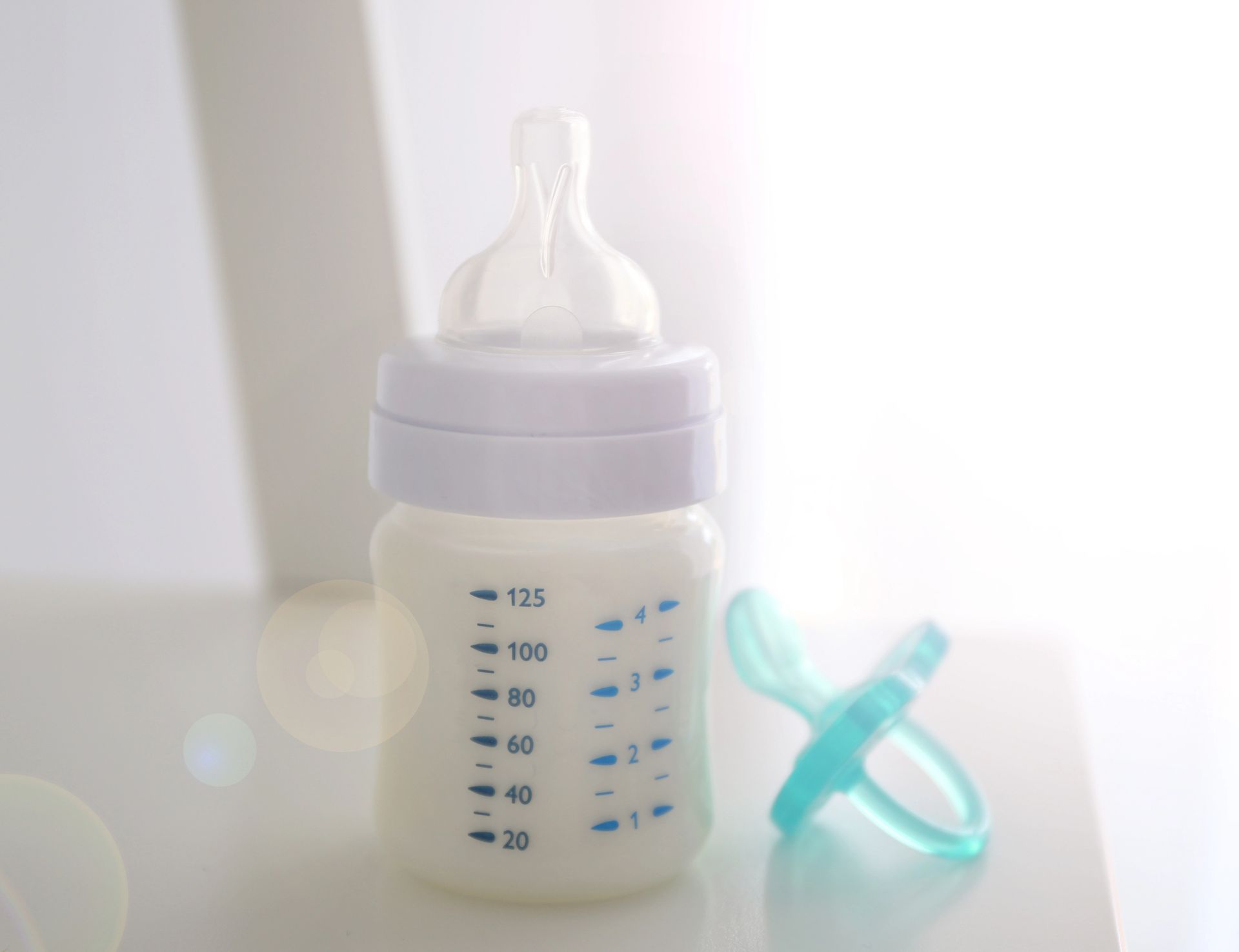 Un biberón lleno de leche y un chupete sobre una mesa.