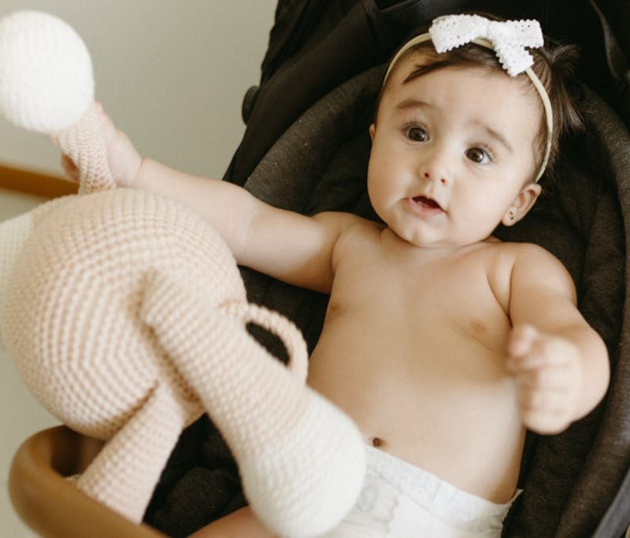 Un bebé con pañal está sentado en un cochecito sosteniendo un animal de peluche.