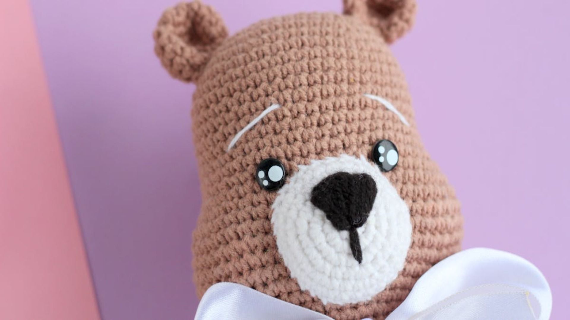 Un primer plano de un osito de peluche tejido a crochet con un lazo blanco.