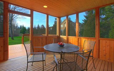 Enclosed wooden porch addition with comfortable seating area overlooking a serene backyard in Rockford, IL, crafted by Forest City Decks.