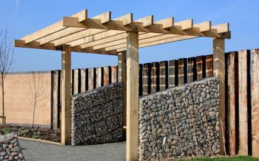 Elegant wooden pergola construction over a stone patio by Forest City Decks enhancing a Rockford, IL residential landscape.